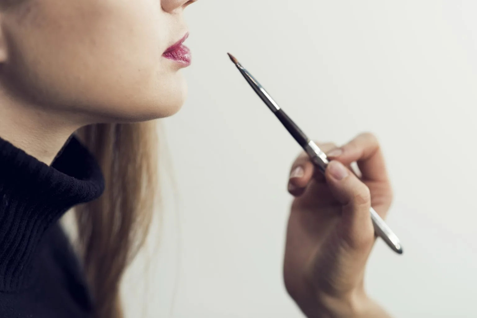 Lip-liner application in profile — blonde client, rose lips, artist hand with fine brush