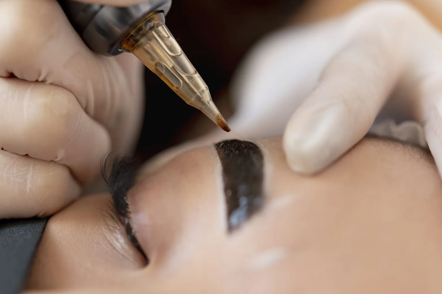 Close macro of a brow being tattooed — defined dark powder brow shape