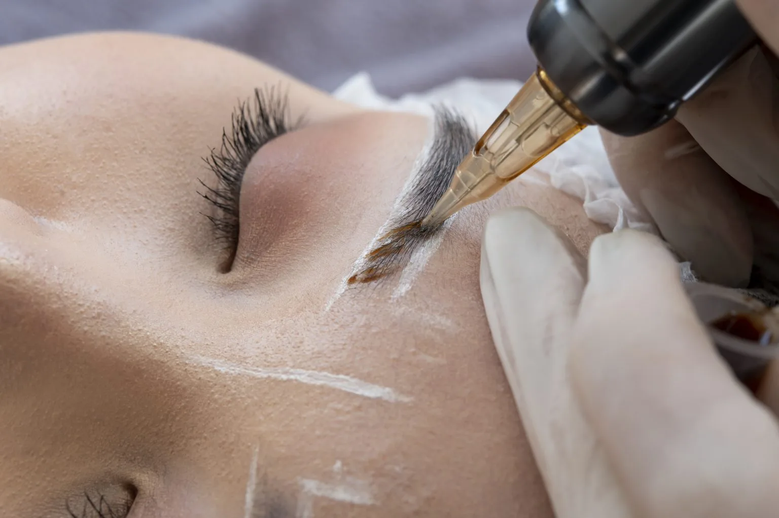 Brow tattoo procedure macro — tattoo machine on a hair-stroked brow