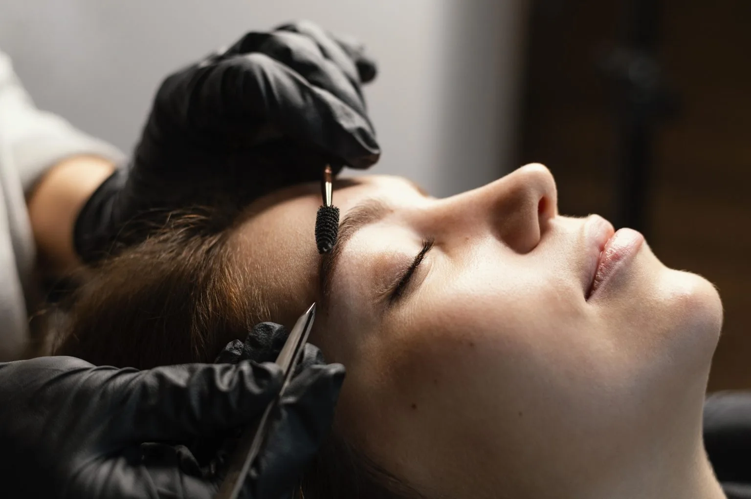 Brow mapping in profile — client reclined eyes-closed, gloved hands with calipers